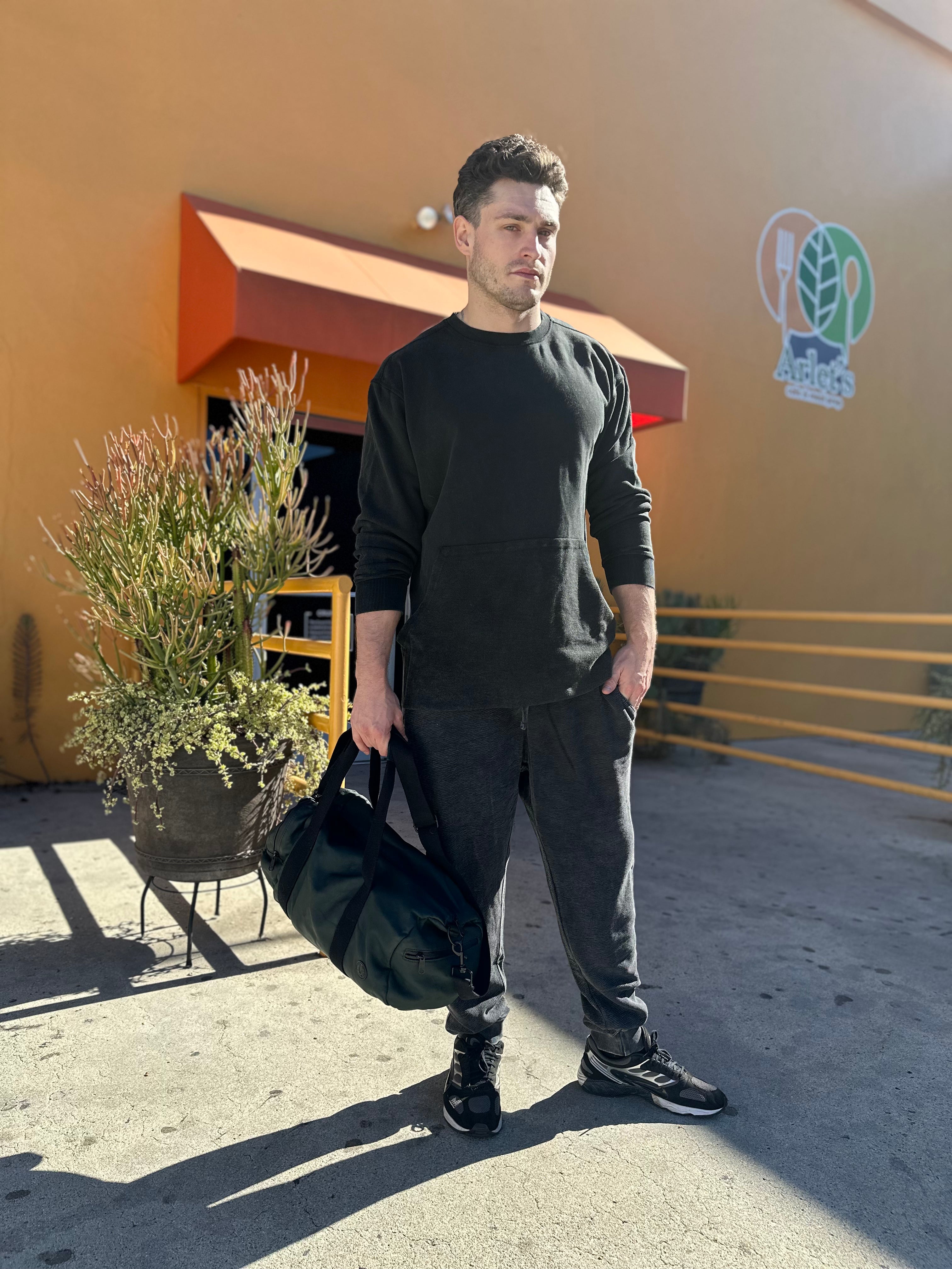 Man in black sweatshirt and pants standing in front of gym.