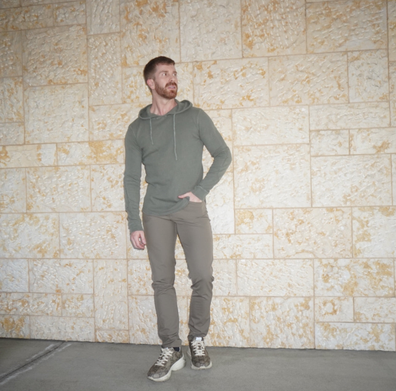 A man in a hoodie and jeans standing in front of a wall.